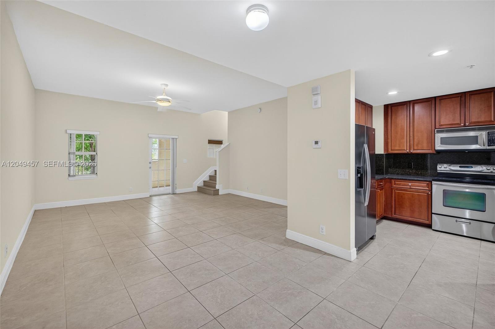 An open-concept living area features tile flooring, a kitchen with wood cabinets, and stairs — 704 SW 1st Ave, Pompano Beach FL 33060, POMPANO BEACH, FL