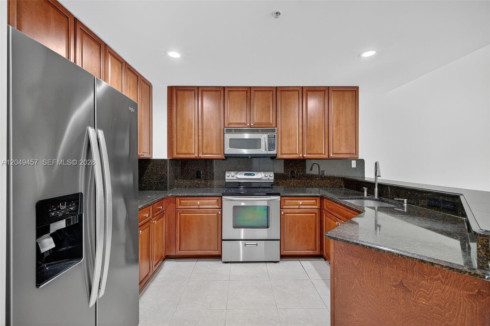 A kitchen features wood cabinets, dark granite countertops, and stainless steel appliances on tiled flooring — 704 SW 1st Ave, Pompano Beach FL 33060, POMPANO BEACH, FL