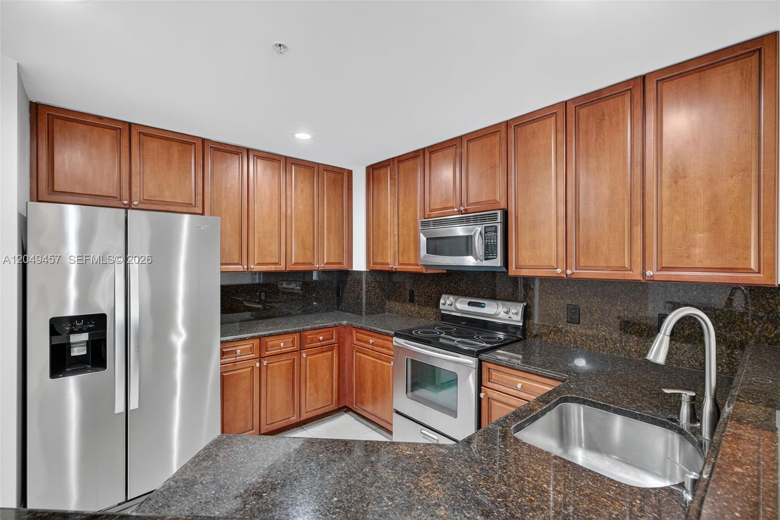 A kitchen features wood cabinets, dark granite countertops, and stainless steel appliances — 704 SW 1st Ave, Pompano Beach FL 33060, POMPANO BEACH, FL