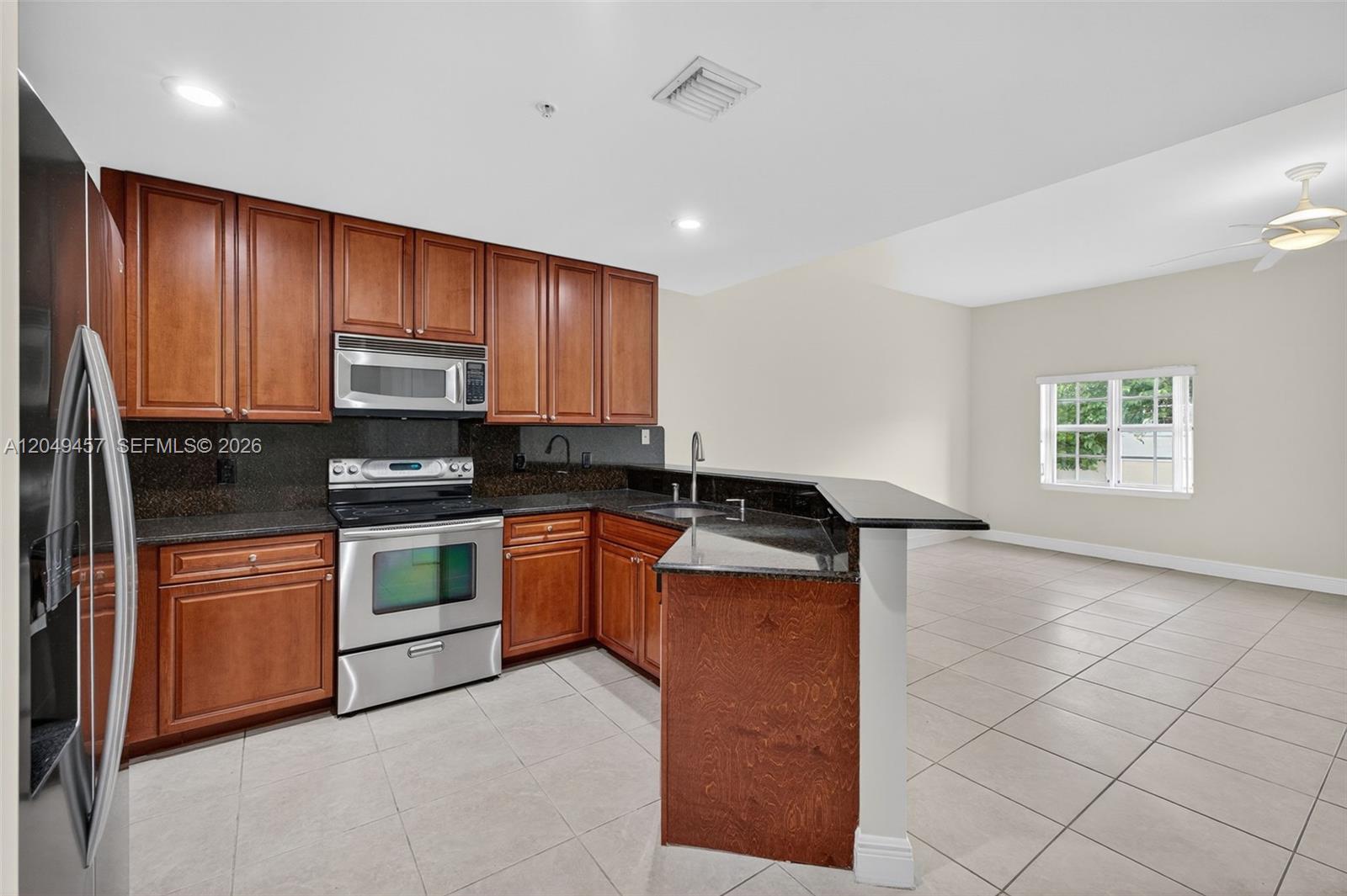 A kitchen features wood cabinets, dark granite countertops, stainless steel appliances, and tile flooring — 704 SW 1st Ave, Pompano Beach FL 33060, POMPANO BEACH, FL
