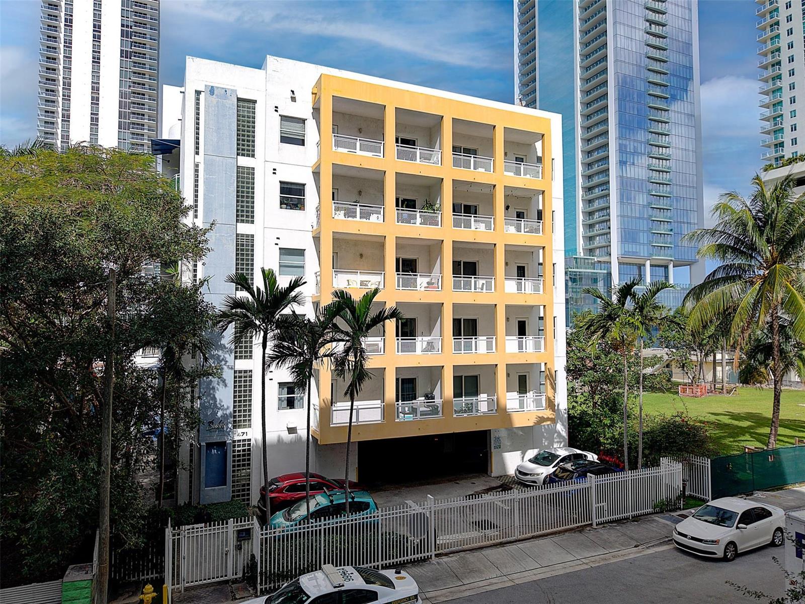 An exterior view of a multi-story apartment building with yellow balconies and a parking area — 471 NE 25th Street # 503, Miami FL 33137, MIAMI, FL