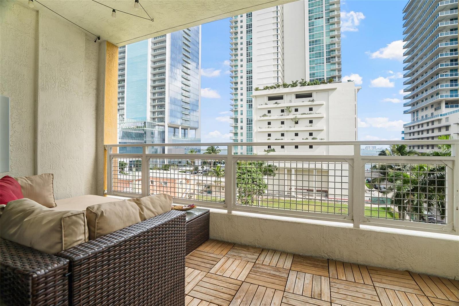 A balcony with wood-tiled flooring, wicker furniture, and a metal railing overlooking city skyscrapers — 471 NE 25th Street # 503, Miami FL 33137, MIAMI, FL