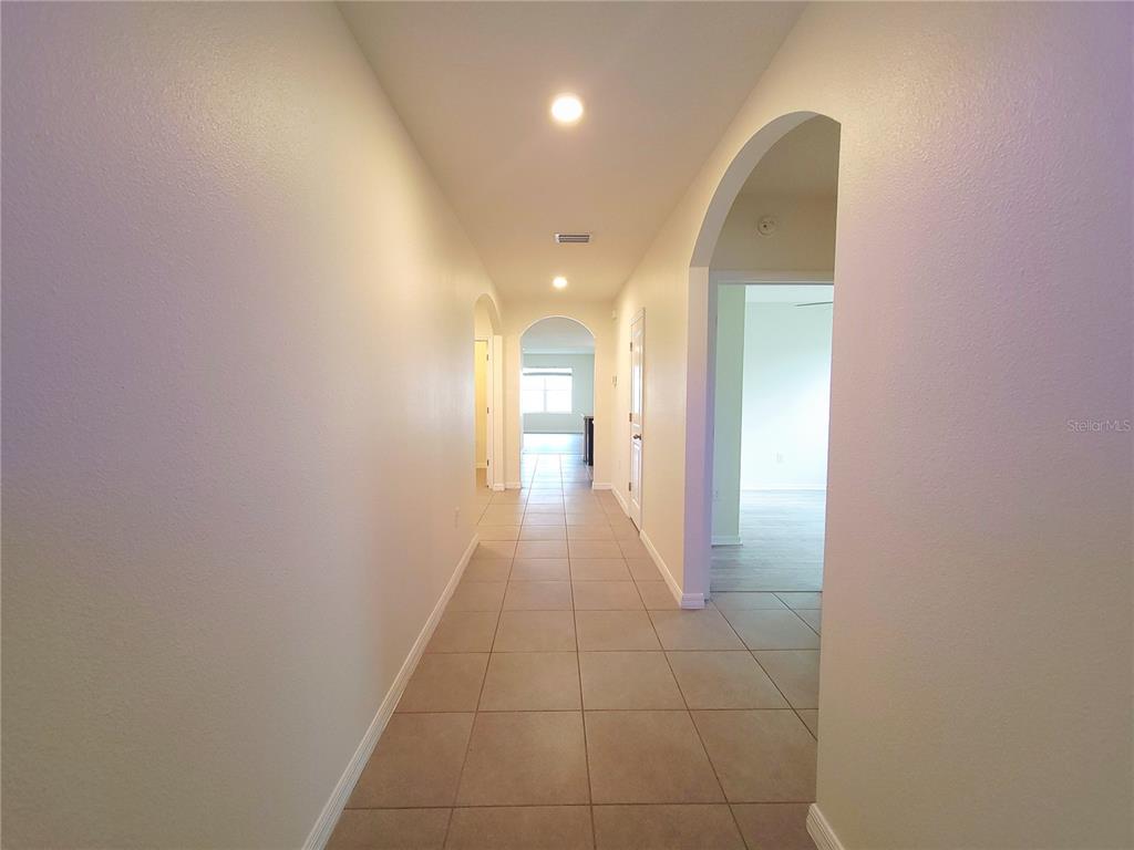A long, tiled hallway features arched doorways and recessed lighting leading toward an open room — 4986 SW 97TH PLACE, OCALA, FL