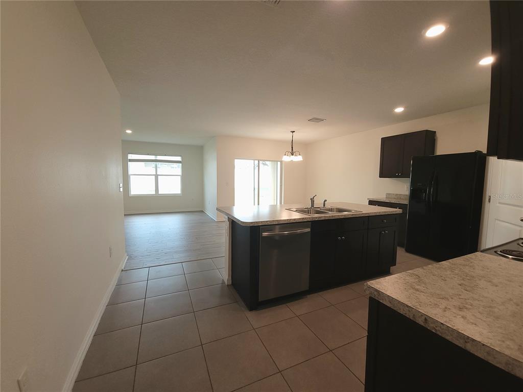 A kitchen with dark cabinets, a central island, and tile flooring opens to a living area — 4986 SW 97TH PLACE, OCALA, FL
