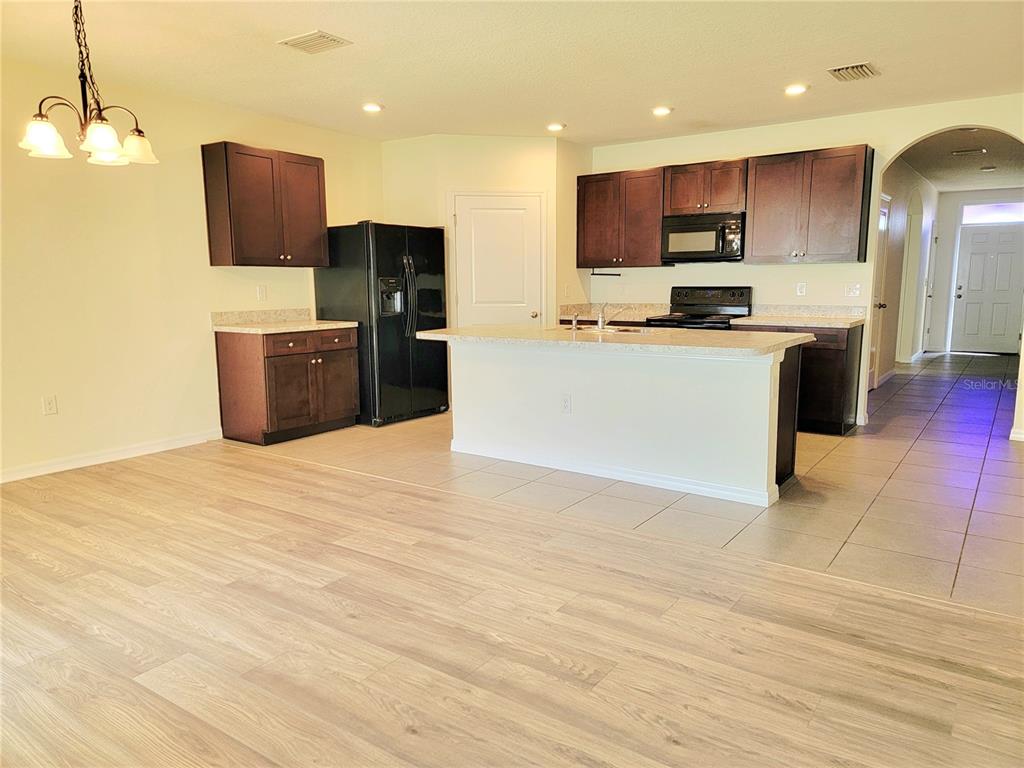 A kitchen features dark wood cabinets, black appliances, a central island, and light-colored flooring — 4986 SW 97TH PLACE, OCALA, FL