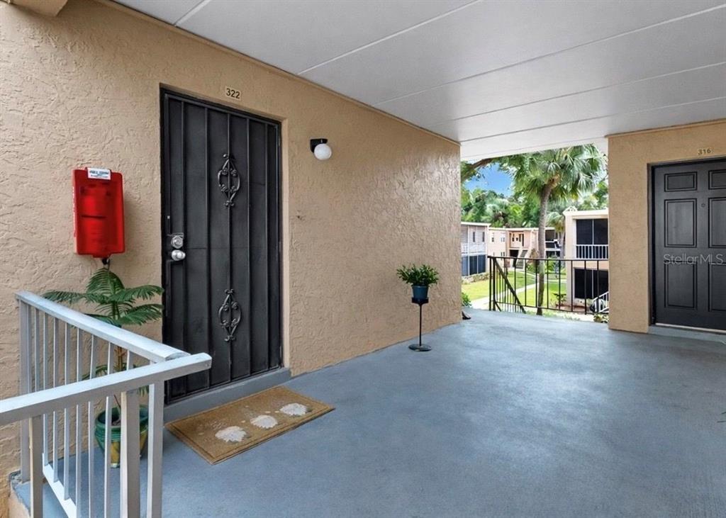 An outdoor apartment walkway features two dark doors, a red fire extinguisher, and railings — 4724 CHRISTA COURT UNIT 322, TAMPA, FL