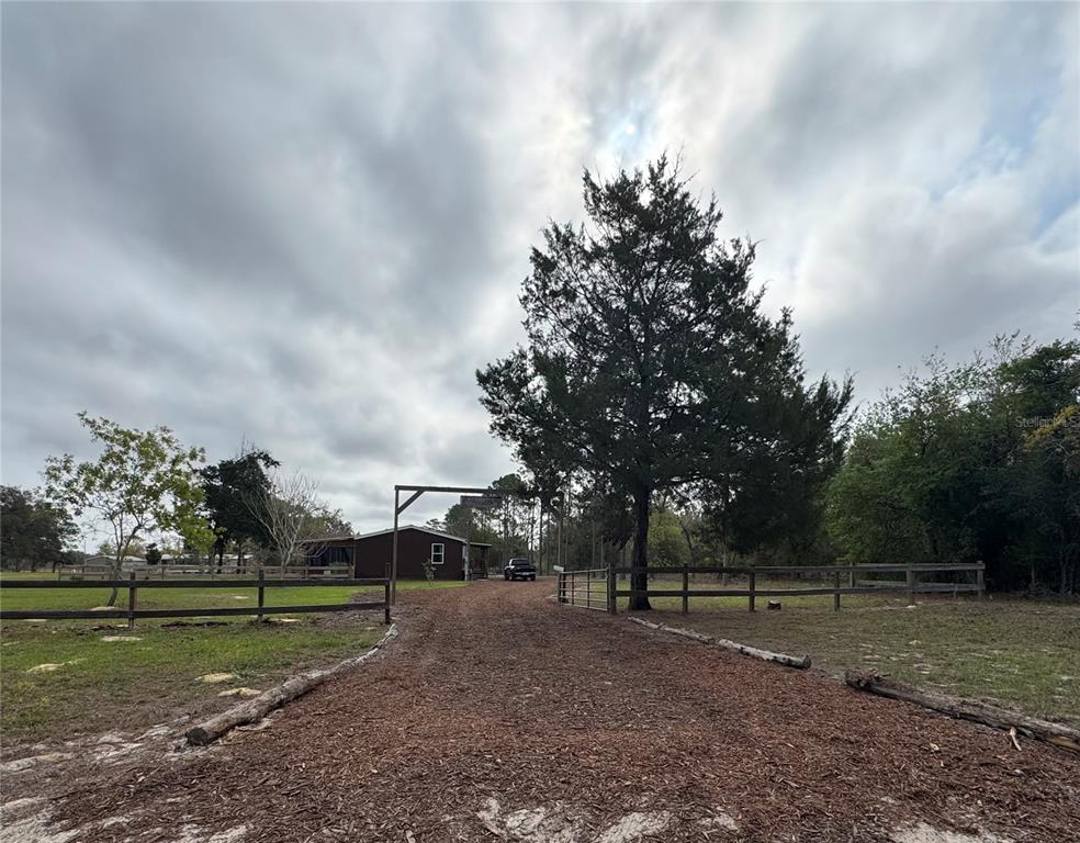 A gravel driveway leads through a wooden gate toward a house under a cloudy sky — 6845 S SUNNYVIEW POINT, HOMOSASSA, FL