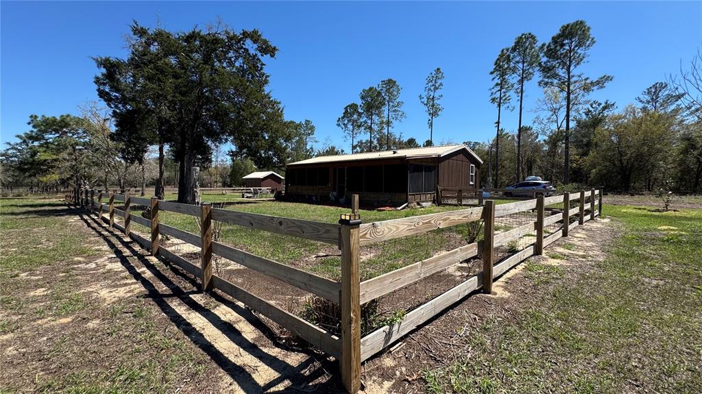 A wooden house with a screened porch sits behind a fenced yard under a clear sky — 6845 S SUNNYVIEW POINT, HOMOSASSA, FL