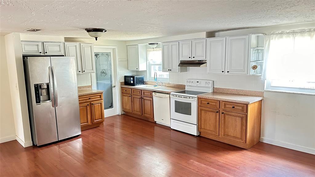 A kitchen features white upper cabinets, wood lower cabinets, stainless steel appliances, and wood flooring — 5891 93RD AVENUE N, PINELLAS PARK, FL