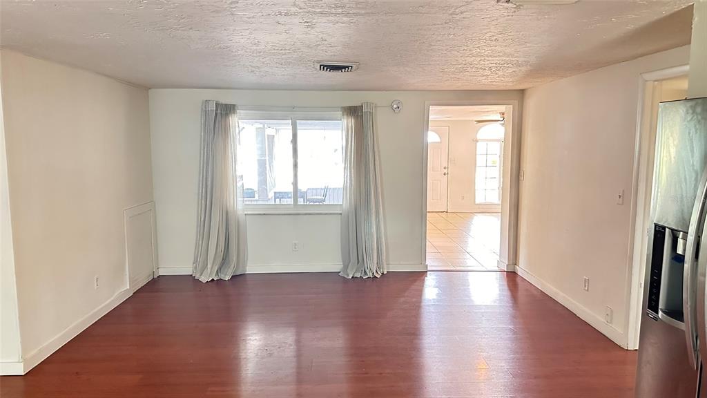 An interior view of a room with reddish-brown wood flooring, a window with curtains, and a doorway — 5891 93RD AVENUE N, PINELLAS PARK, FL