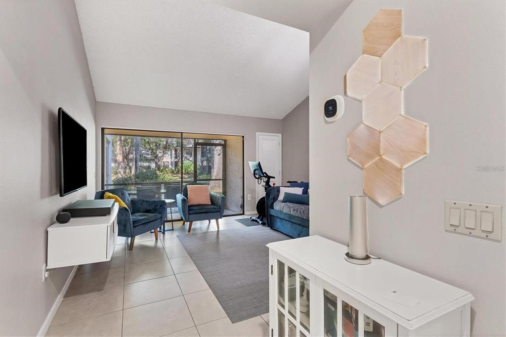 A living room features tile floors, a wall-mounted television, blue armchairs, and hexagonal wall decor — 4717 WINSLOW BEACON UNIT 7, SARASOTA, FL