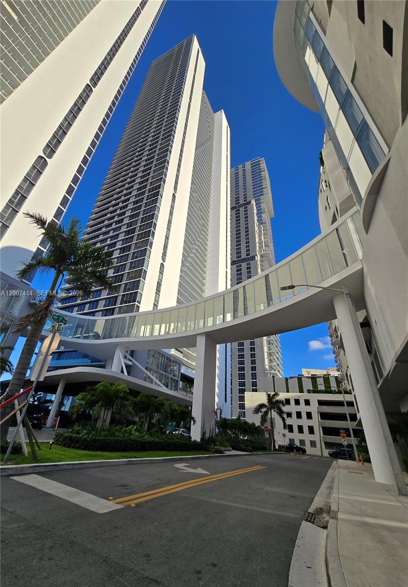 A low-angle view shows a glass pedestrian bridge connecting two modern high-rise buildings — 700 NE 24 ST # 3104, Miami FL 33137, MIAMI, FL