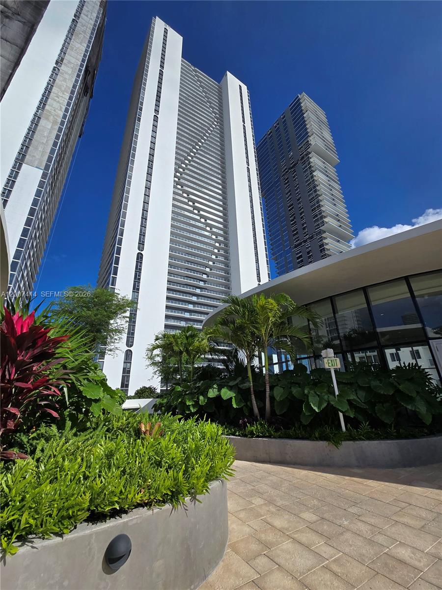 A low-angle view shows a modern white skyscraper and a glass-walled building with landscaping — 700 NE 24 ST # 3104, Miami FL 33137, MIAMI, FL