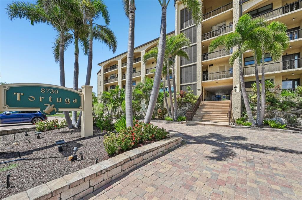A multi-story apartment building features a paved entrance, palm trees, and a prominent sign — 8710 MIDNIGHT PASS ROAD UNIT 203B, SARASOTA, FL