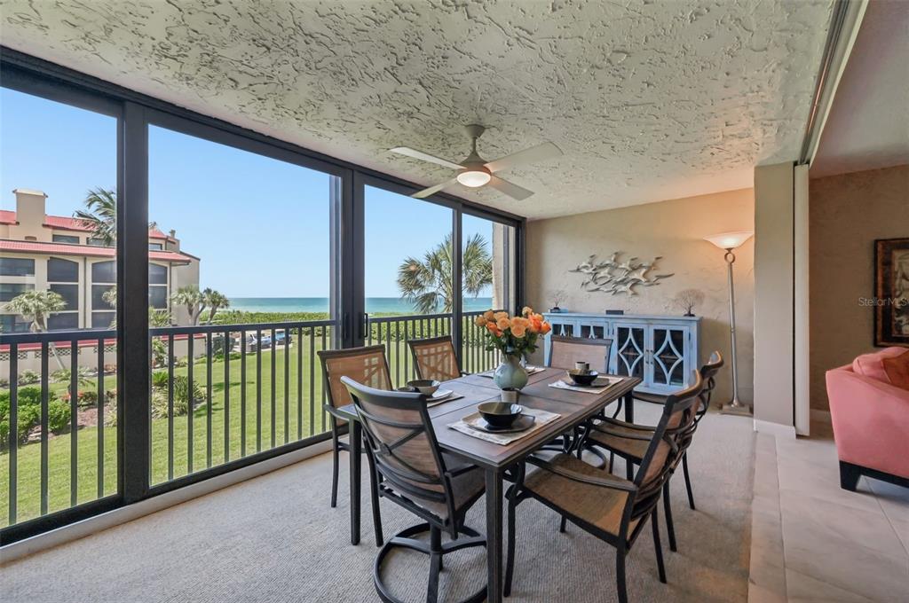 A dining area on a screened-in balcony features a table, chairs, and ocean views — 8710 MIDNIGHT PASS ROAD UNIT 203B, SARASOTA, FL