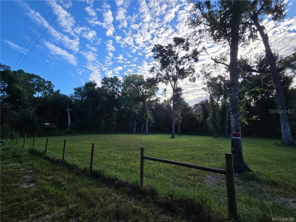 A fenced, grassy lot is surrounded by mature trees under a blue sky with clouds — 4713 S IRONWOOD POINT, INVERNESS, FL