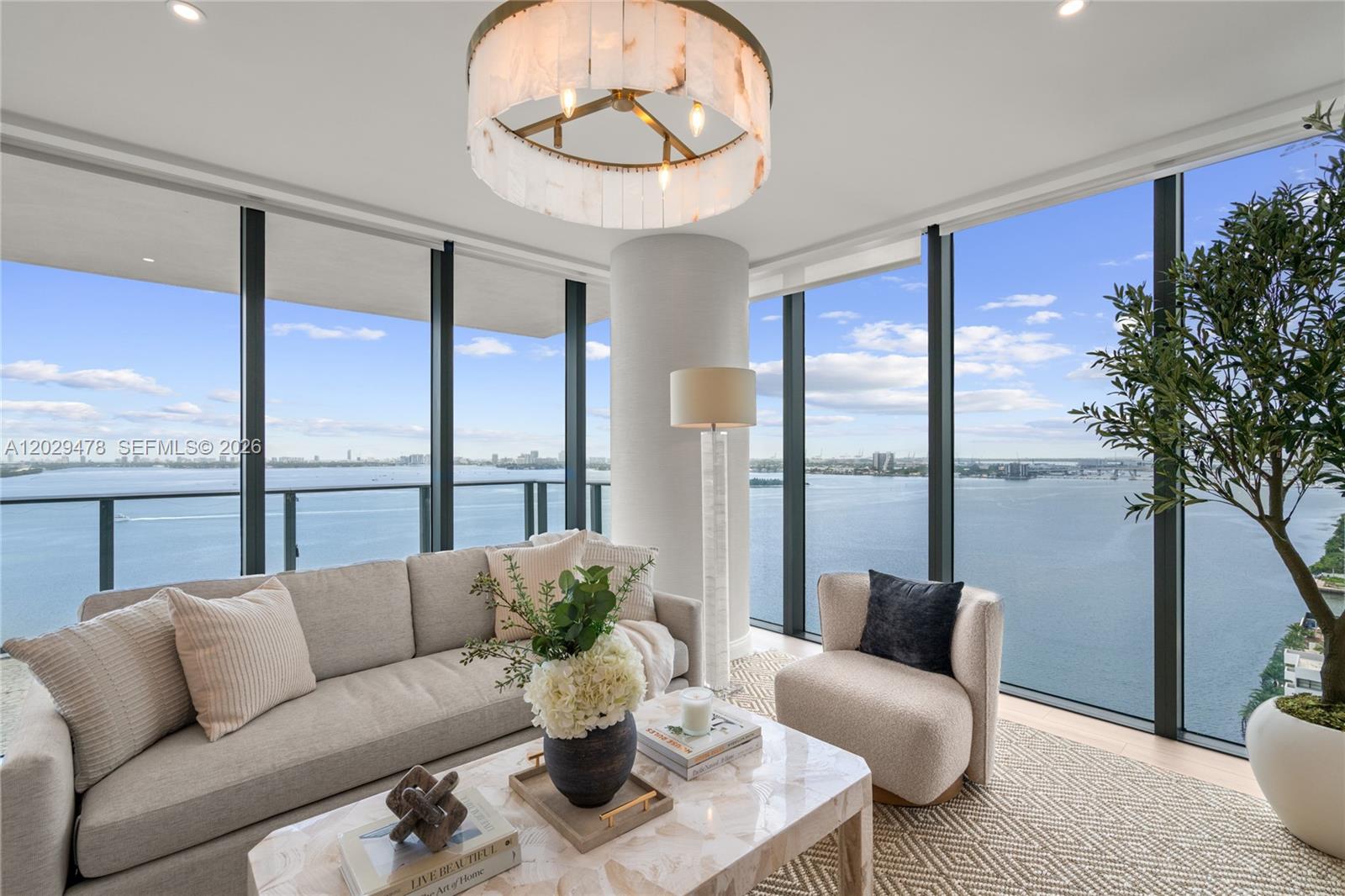 A modern living room features a sofa, armchair, and floor-to-ceiling windows overlooking the water — 3131 NE 7th Ave # 2101, Miami FL 33137, MIAMI, FL
