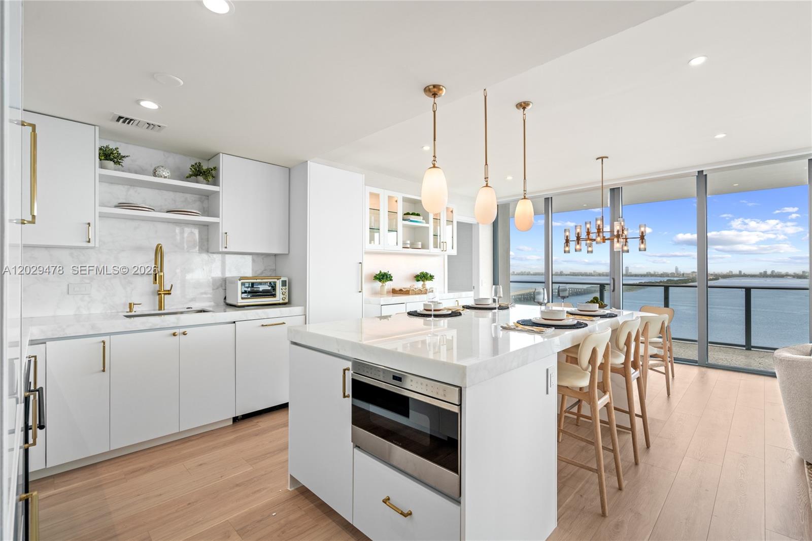 A modern white kitchen features a marble island, gold hardware, and floor-to-ceiling water views — 3131 NE 7th Ave # 2101, Miami FL 33137, MIAMI, FL