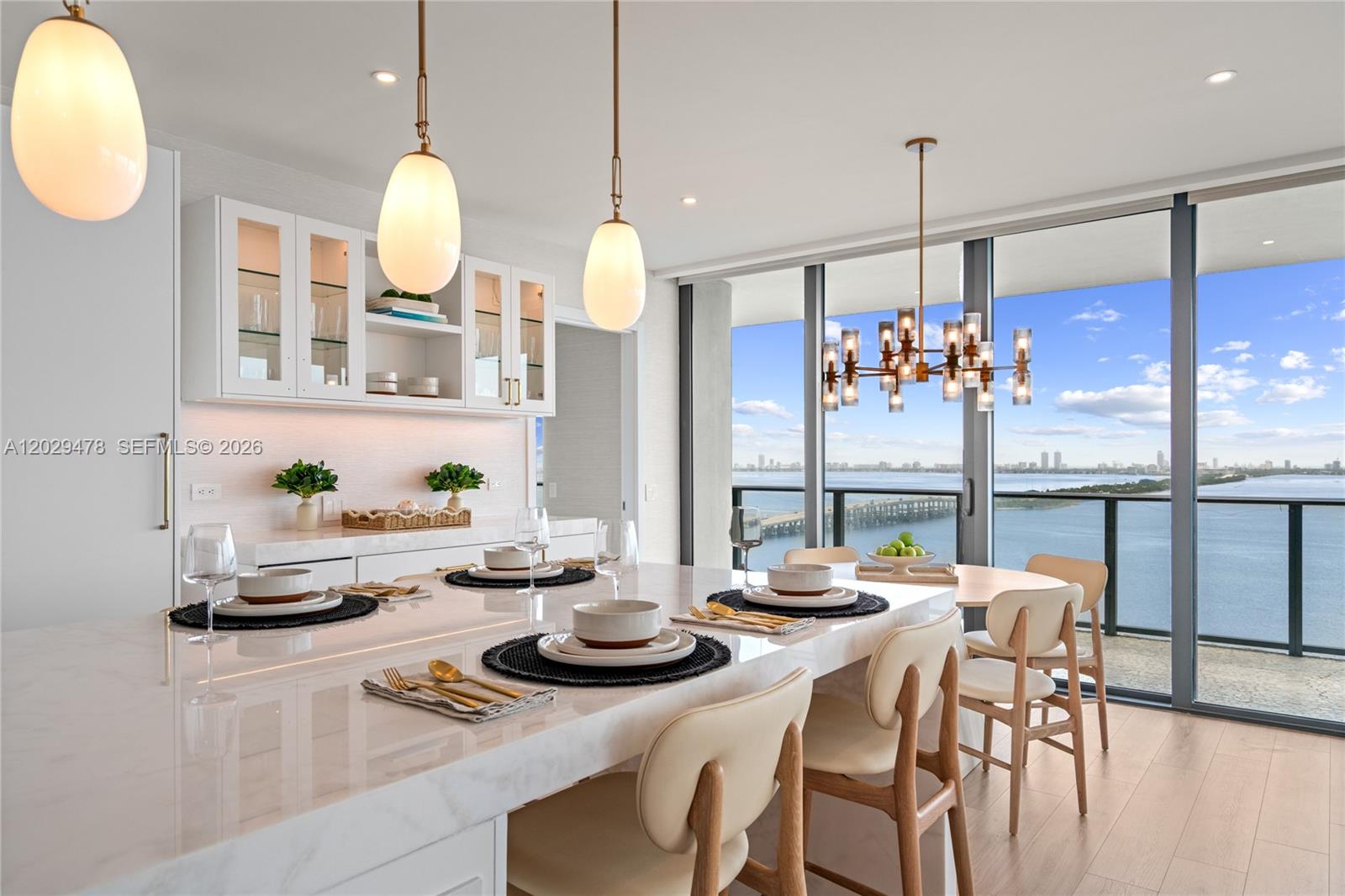 A modern dining area features a marble island, pendant lighting, and floor-to-ceiling windows overlooking water — 3131 NE 7th Ave # 2101, Miami FL 33137, MIAMI, FL