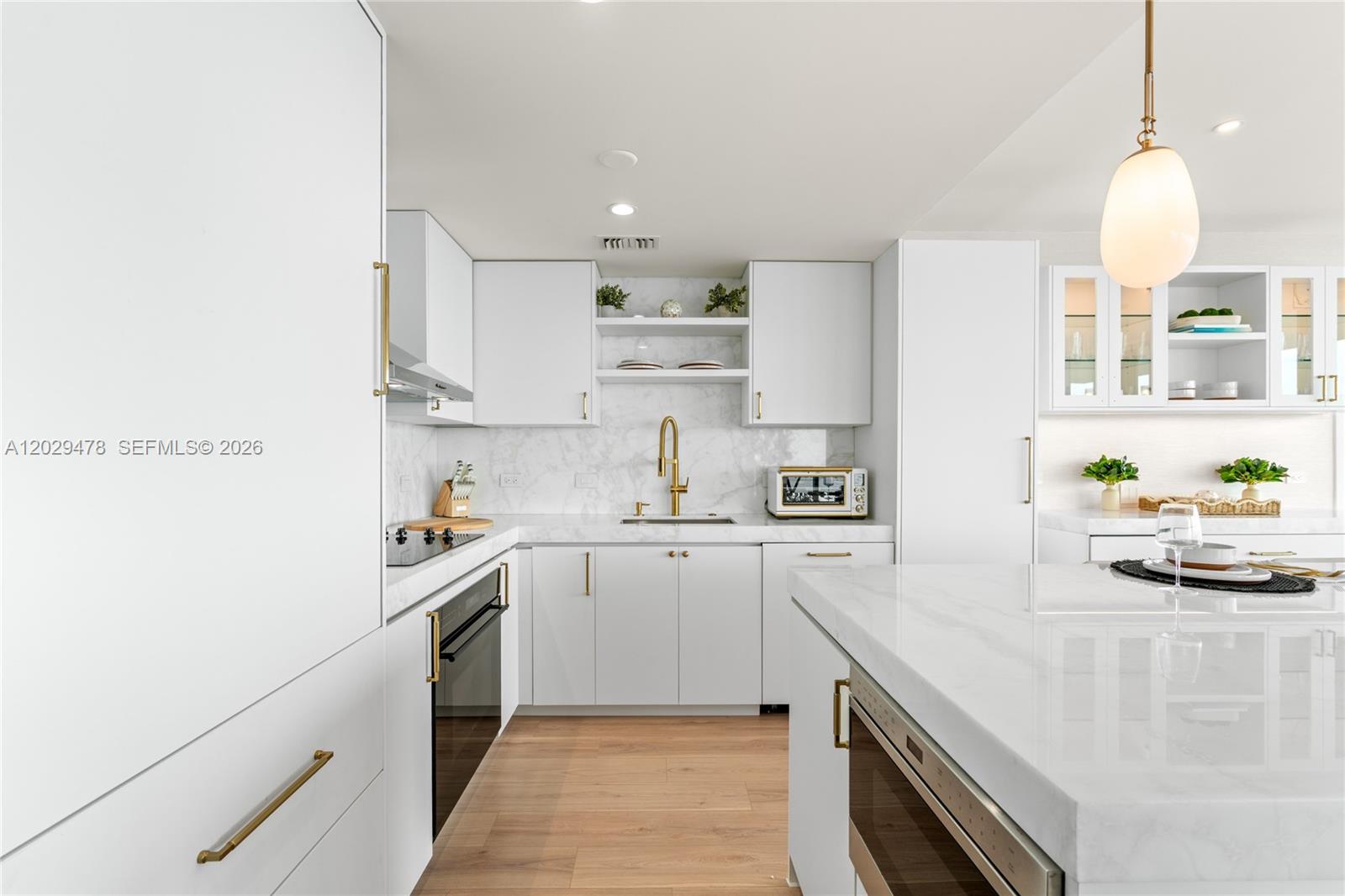 A modern white kitchen features marble countertops, gold hardware, and light wood flooring — 3131 NE 7th Ave # 2101, Miami FL 33137, MIAMI, FL
