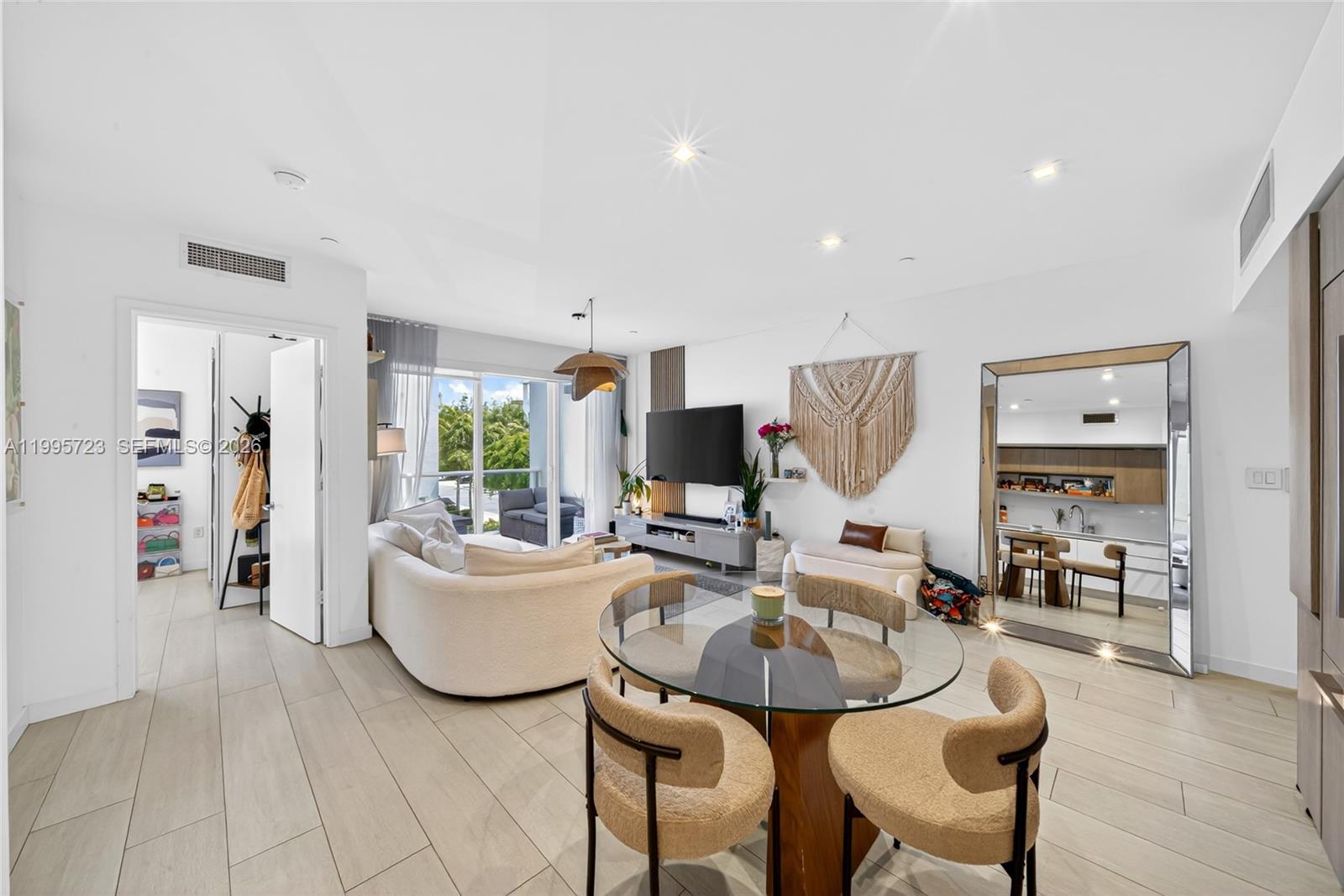 A modern living and dining area features a glass table, curved sofa, and large mirror — 455 NE 39th St # 113, Miami FL 33137, MIAMI, FL
