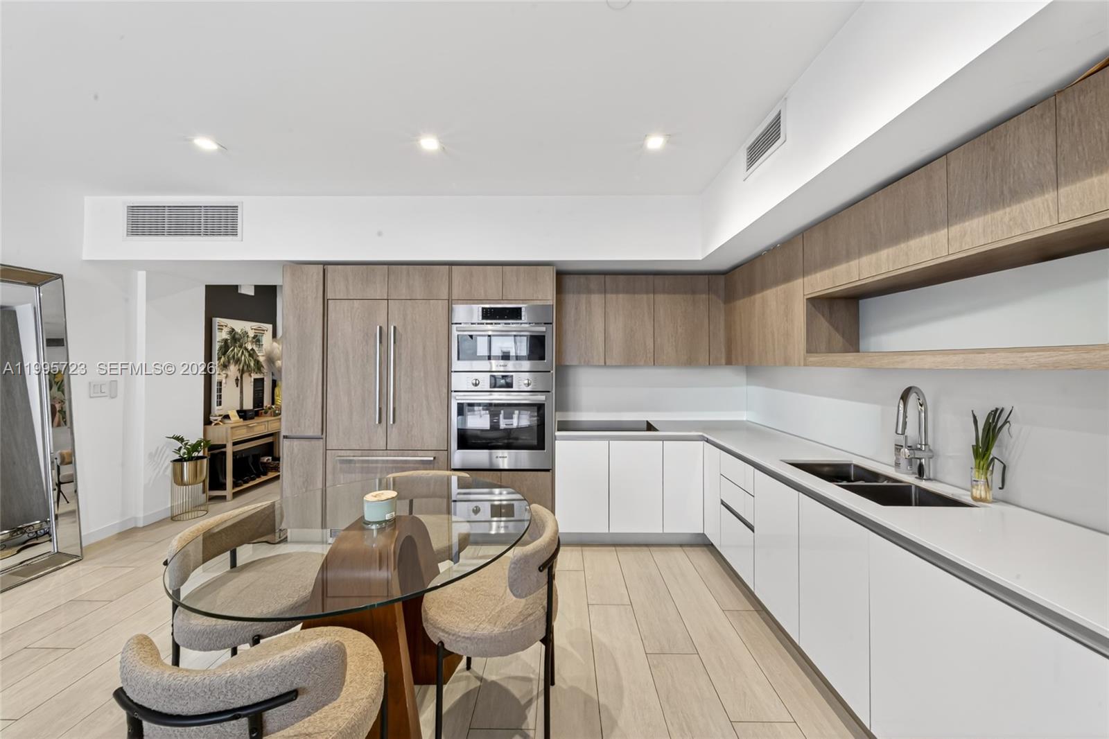 A modern kitchen features white lower cabinets, wood-toned upper cabinetry, and a glass dining table — 455 NE 39th St # 113, Miami FL 33137, MIAMI, FL