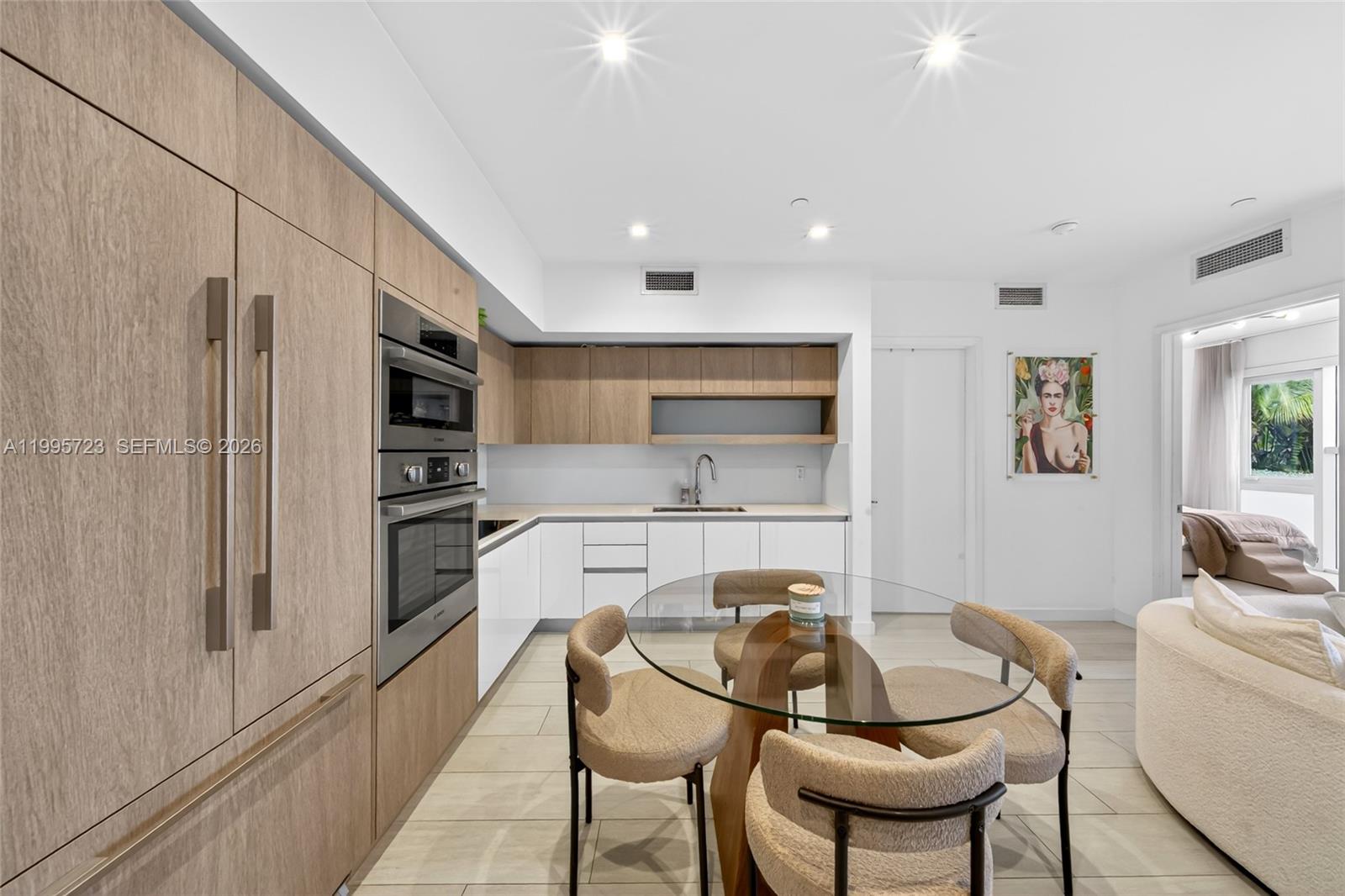 A modern kitchen features light wood cabinetry, white lower cabinets, and a glass dining table — 455 NE 39th St # 113, Miami FL 33137, MIAMI, FL