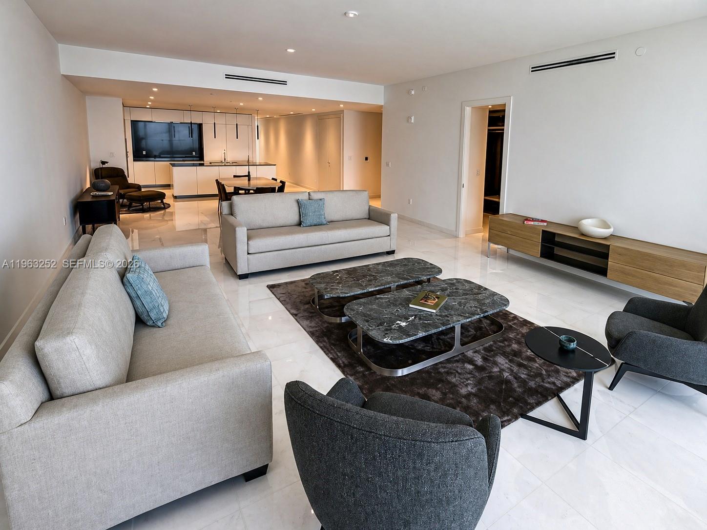 A modern living room features light-colored sofas, marble coffee tables, and an open kitchen area — 300 Biscayne Blvd Way # 4404, Miami FL 33131, MIAMI, FL