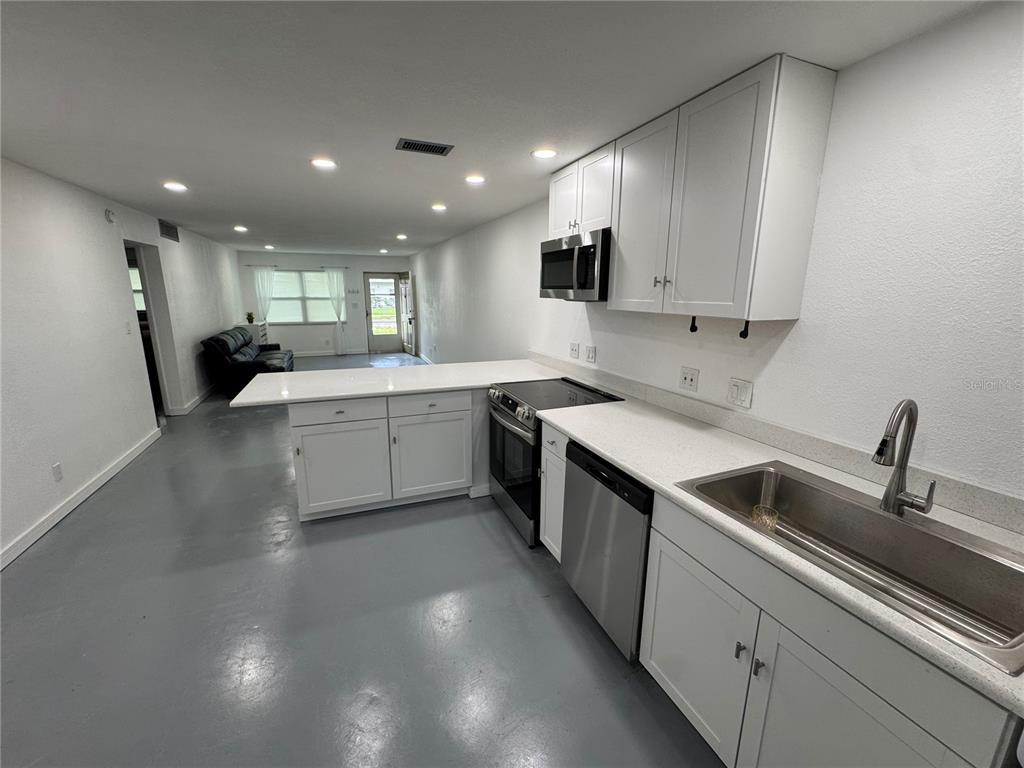 A kitchen with white cabinets, stainless steel appliances, and gray flooring opens to a living area — 5720 13TH AVENUE N UNIT 106B, ST PETERSBURG, FL