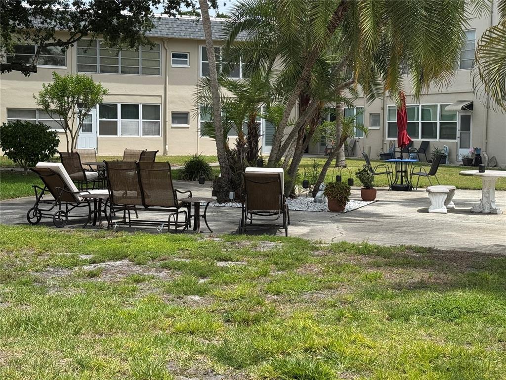 A paved courtyard features outdoor seating, potted plants, and palm trees in front of apartments — 5720 13TH AVENUE N UNIT 106B, ST PETERSBURG, FL
