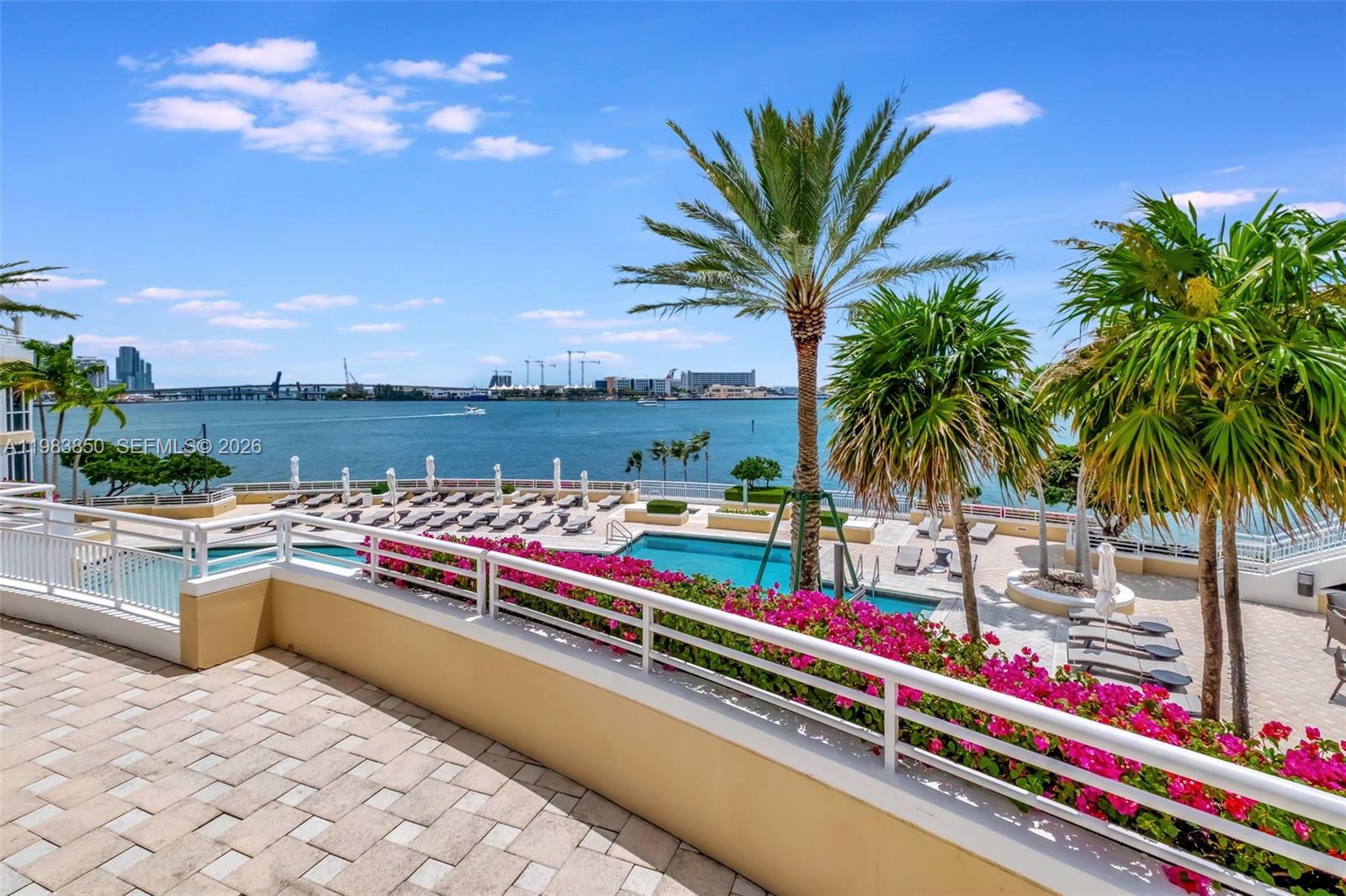 A balcony overlooks a swimming pool, palm trees, and a bay with a distant city skyline — 848 Brickell Key Dr # 2602, Miami FL 33131, MIAMI, FL