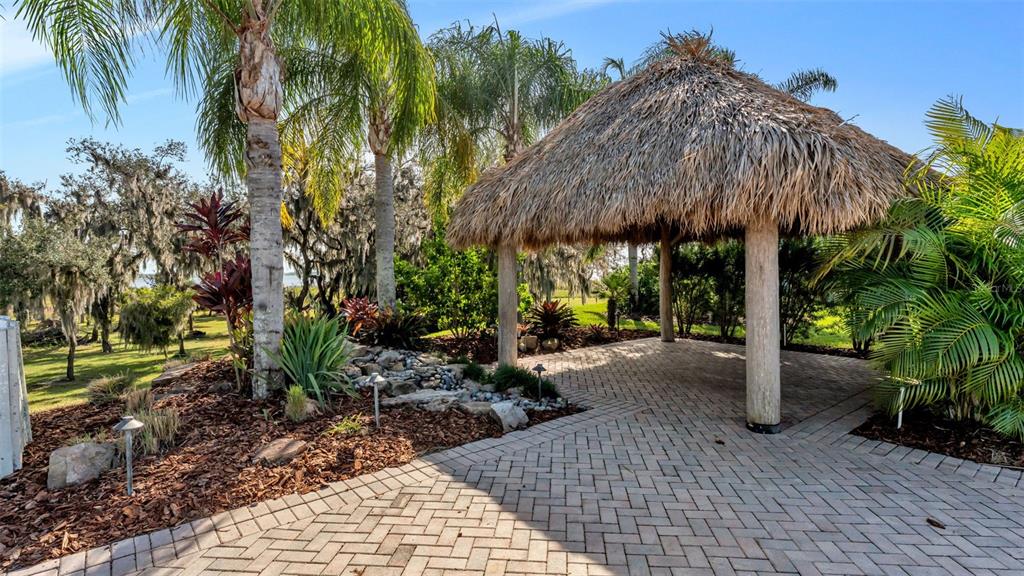 A thatched-roof tiki hut sits on a brick patio surrounded by palm trees and landscaping — 3312 FISH HAWK DRIVE, POLK CITY, FL