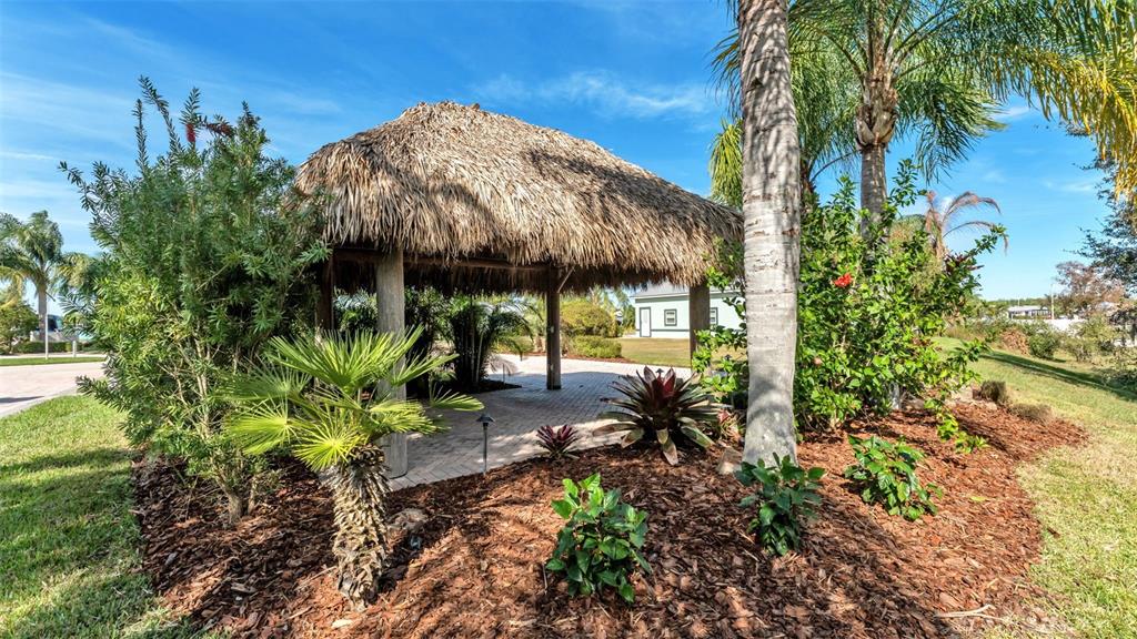 A thatched-roof tiki hut stands in a landscaped yard with mulch and tropical plants — 3312 FISH HAWK DRIVE, POLK CITY, FL