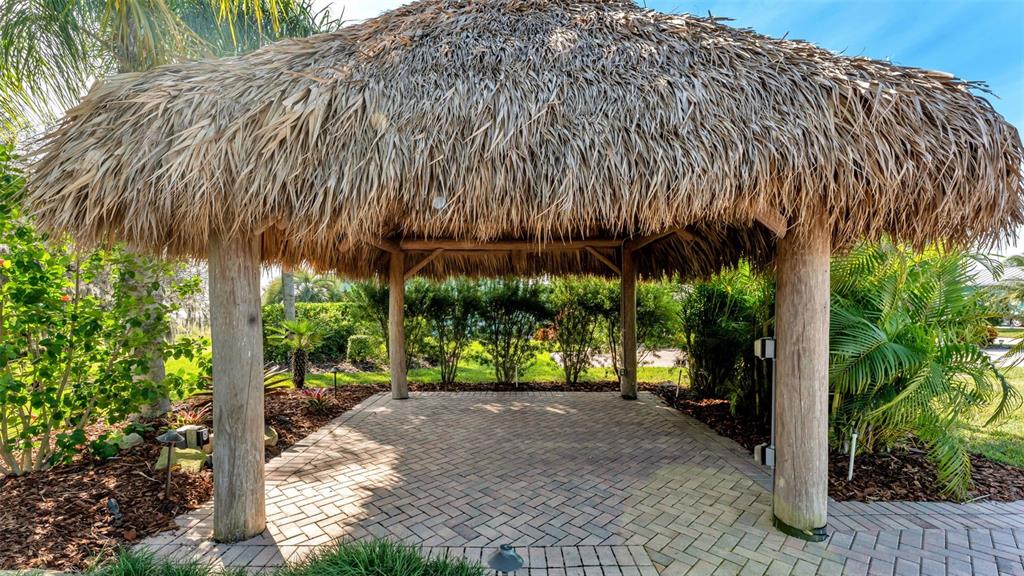 A thatched-roof tiki hut stands over a brick-paved patio surrounded by tropical landscaping — 3312 FISH HAWK DRIVE, POLK CITY, FL