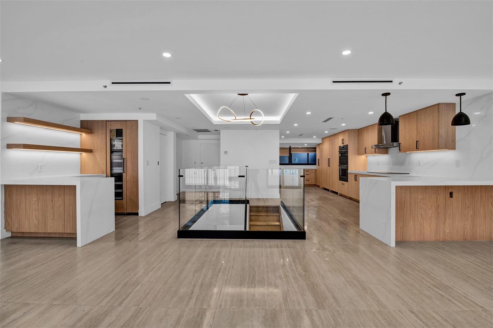 A modern kitchen features wood cabinetry, white marble countertops, and a glass-enclosed staircase — 520 E Brickell Key Drive, Miami FL 33131, MIAMI, FL