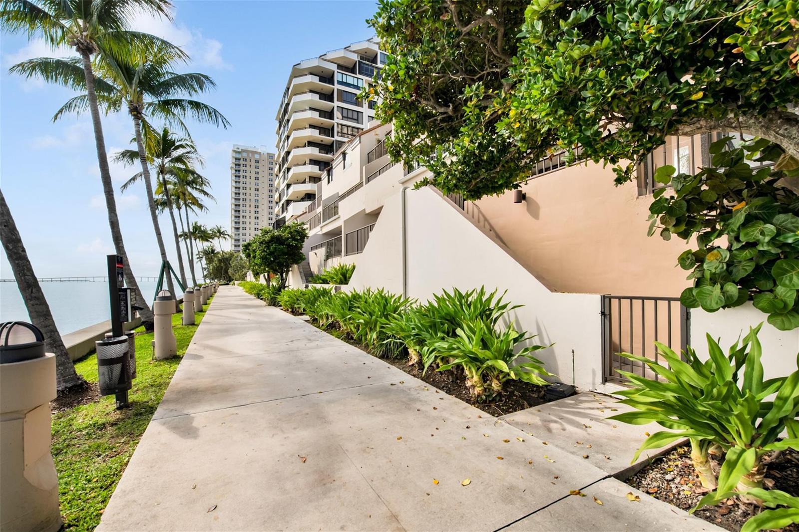 A concrete walkway runs alongside a multi-story building, palm trees, and a waterfront view — 520 E Brickell Key Drive, Miami FL 33131, MIAMI, FL