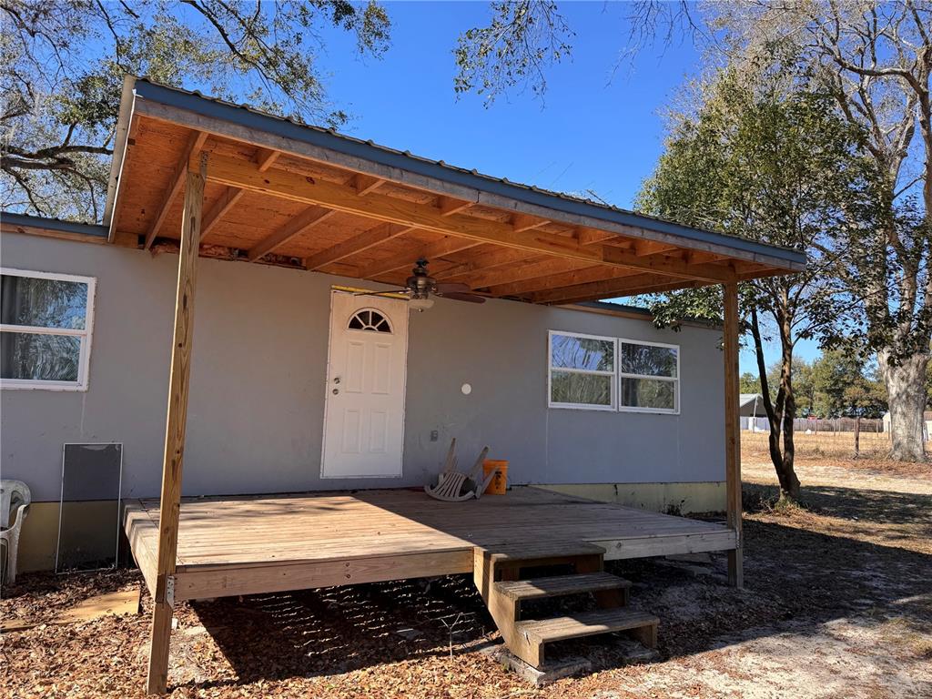 A wooden deck with a covered porch and stairs sits in front of a house — 7647 SHANNON LANE, ZEPHYRHILLS, FL