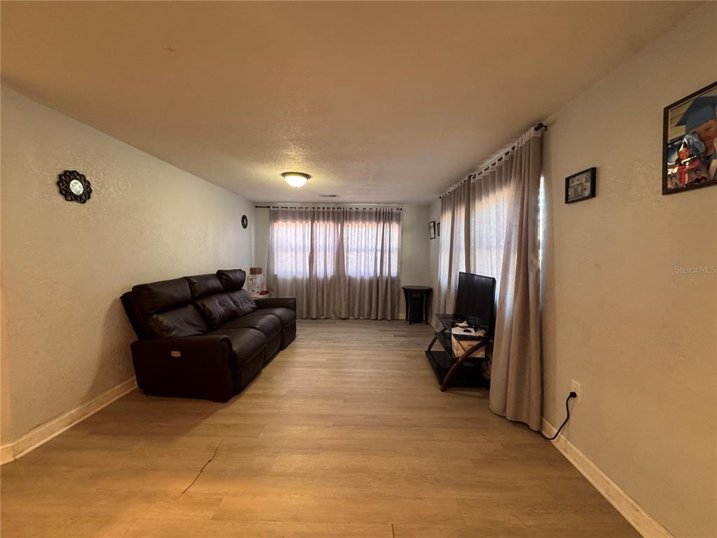 A living room features light wood-look flooring, a dark leather sofa, and floor-to-ceiling curtains — 7647 SHANNON LANE, ZEPHYRHILLS, FL