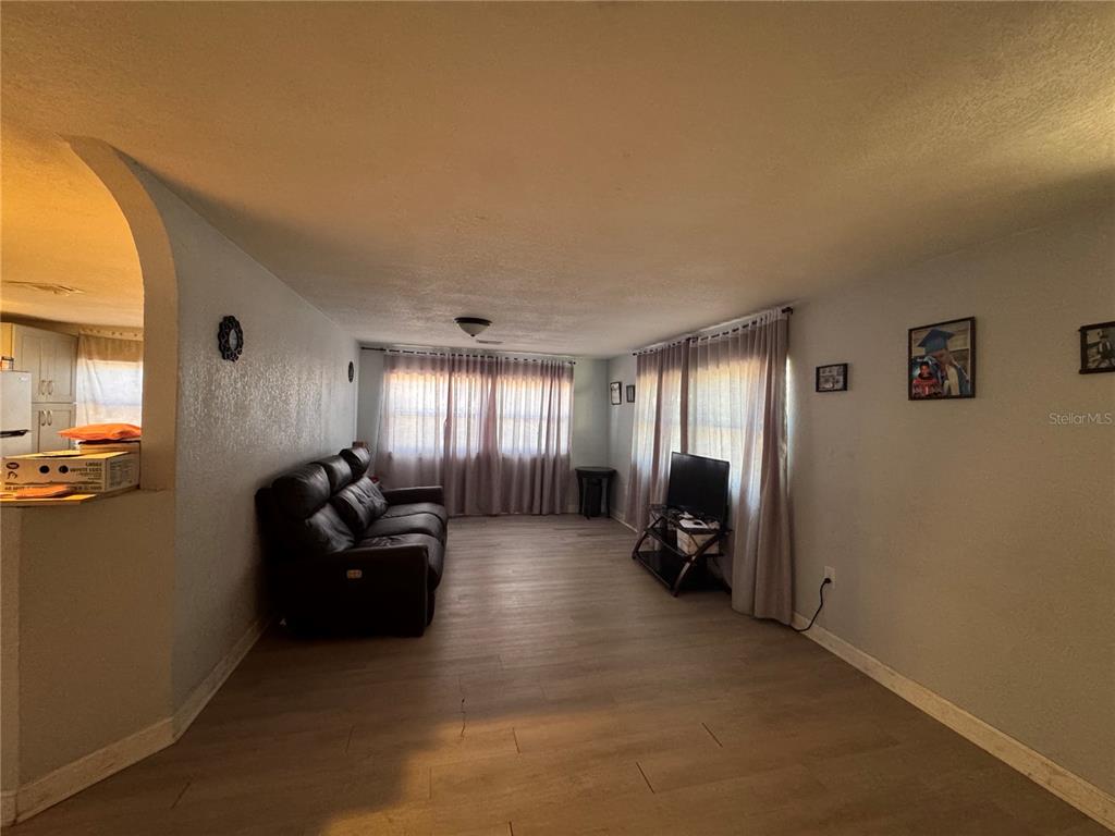 A living room features light wood-look flooring, a dark leather sofa, and floor-to-ceiling curtains — 7647 SHANNON LANE, ZEPHYRHILLS, FL