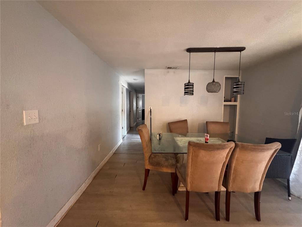 A dining area features a glass table, upholstered chairs, pendant lights, and light wood flooring — 7647 SHANNON LANE, ZEPHYRHILLS, FL