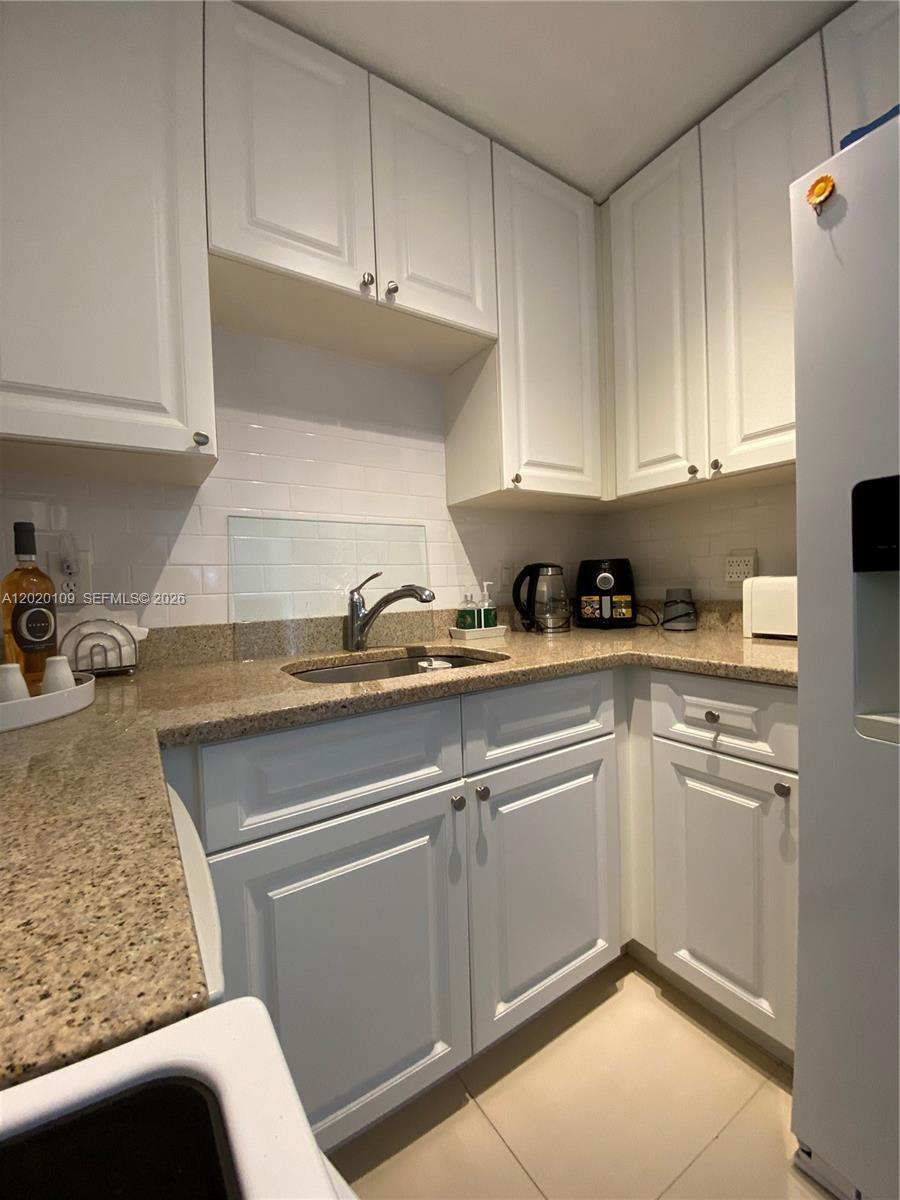 A small kitchen features white cabinets, granite countertops, and a stainless steel sink — 5050 NW 7th St # 312, Miami FL 33126, MIAMI, FL