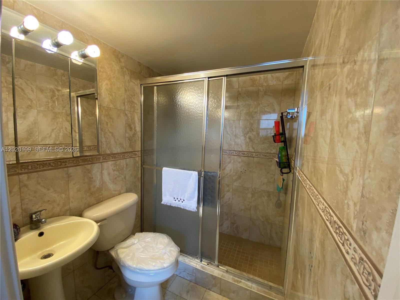 A bathroom features beige tiled walls, a pedestal sink, a toilet, and a glass shower — 5050 NW 7th St # 312, Miami FL 33126, MIAMI, FL