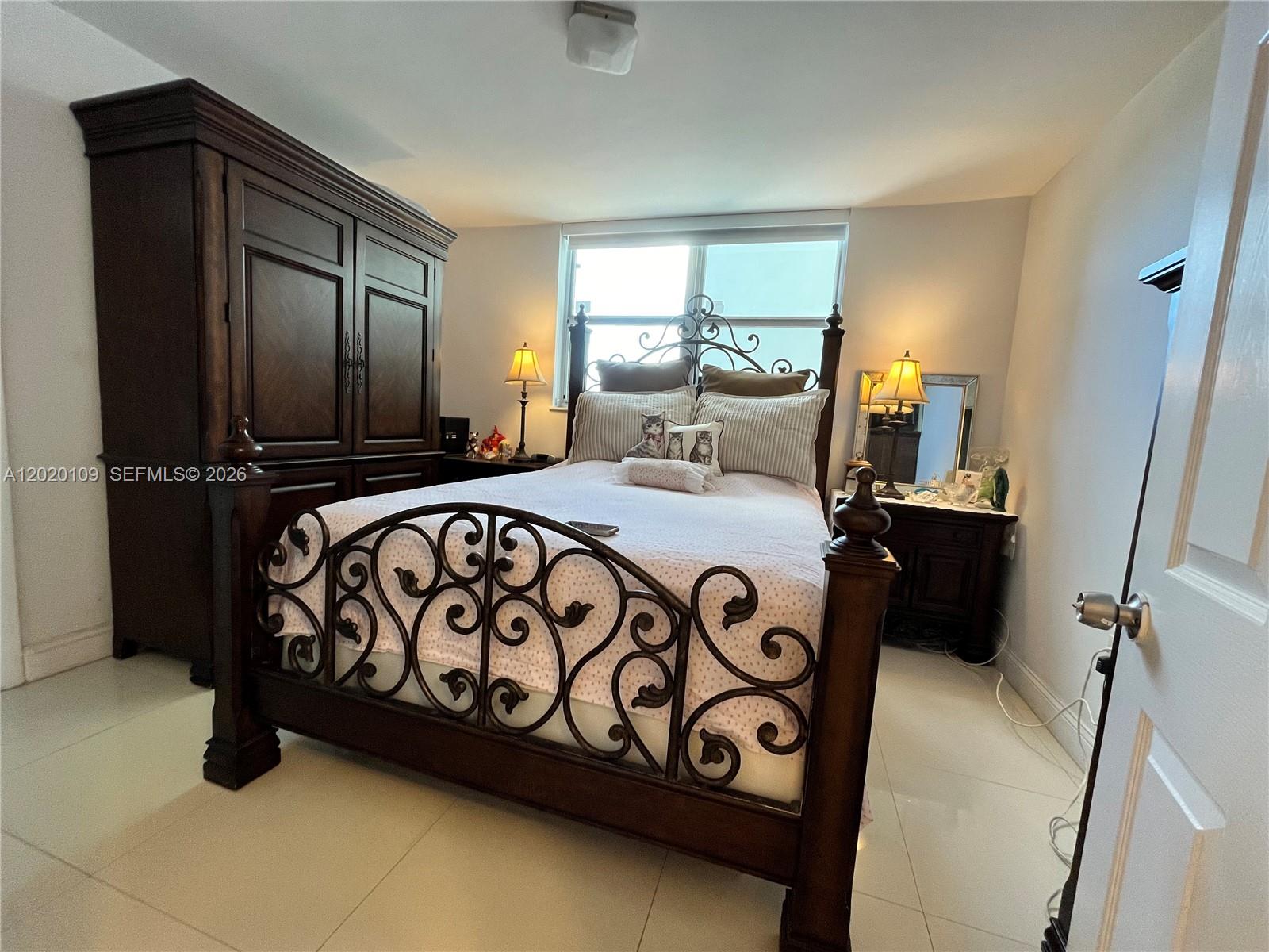A bedroom features a dark wood bed frame with metal scrollwork, matching furniture, and tile flooring — 5050 NW 7th St # 312, Miami FL 33126, MIAMI, FL