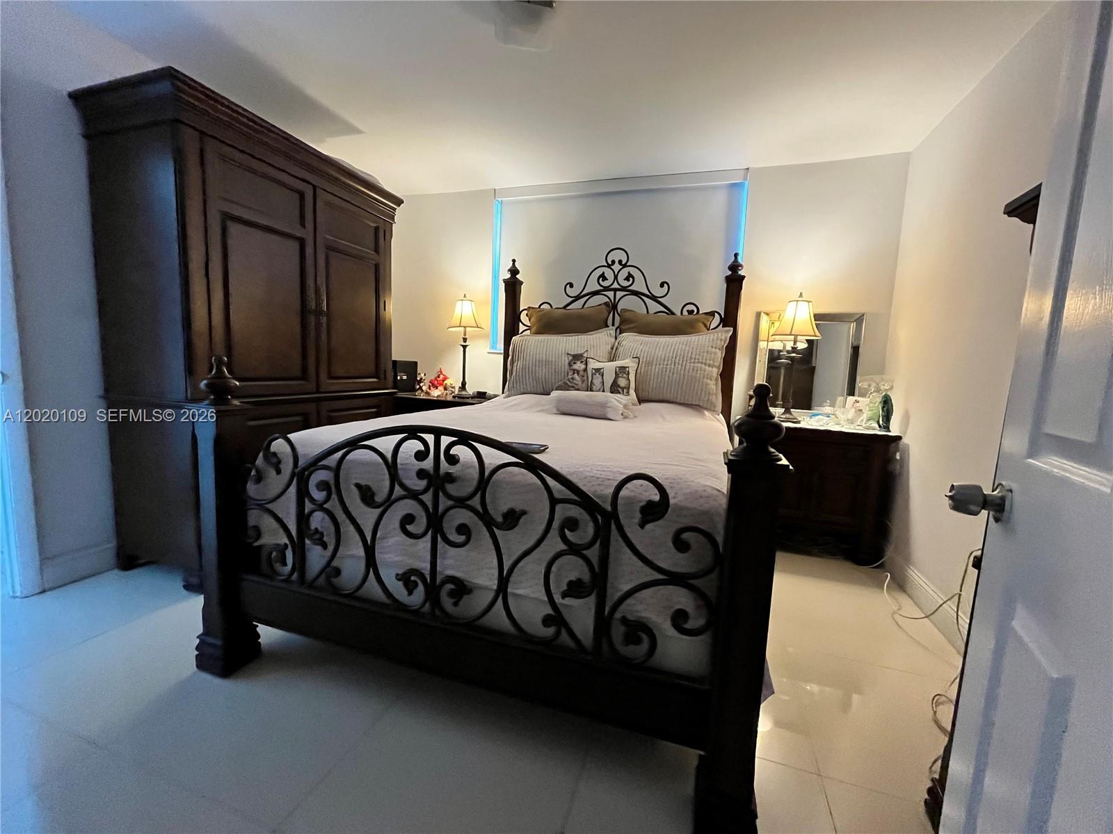 A bedroom features a dark wood and wrought iron bed frame, wardrobe, and tile flooring — 5050 NW 7th St # 312, Miami FL 33126, MIAMI, FL