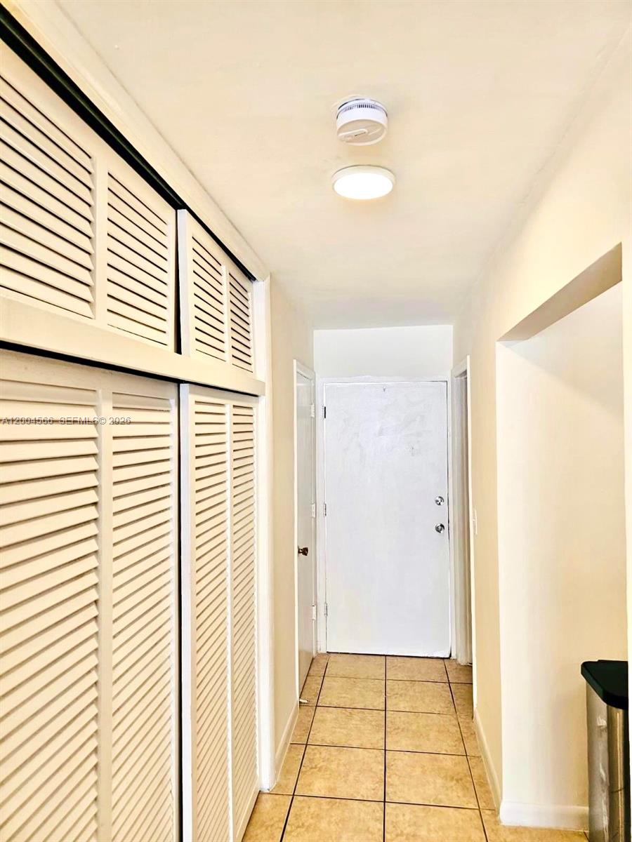 A hallway features white louvered closet doors, beige tile flooring, and a ceiling light fixture — 1441 Lincoln Rd # 212, Miami Beach FL 33139, MIAMI BEACH, FL