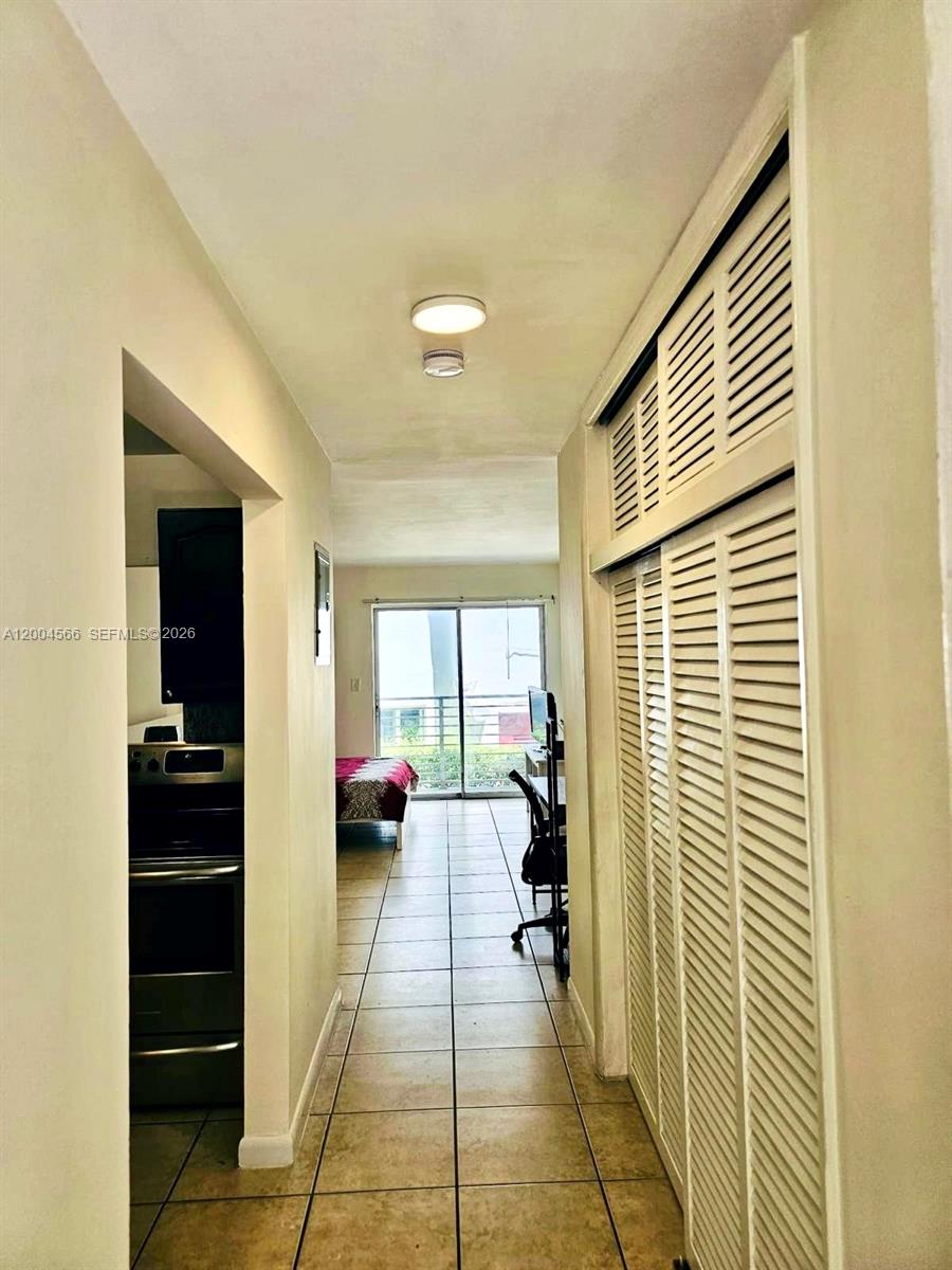 A hallway with tile flooring leads to a bedroom with a sliding glass door — 1441 Lincoln Rd # 212, Miami Beach FL 33139, MIAMI BEACH, FL