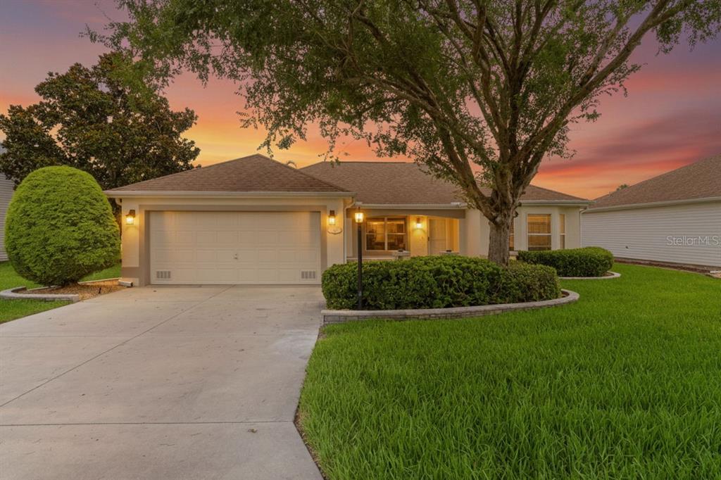 A single-story house with a two-car garage, a large tree, and a landscaped front yard — 1213 EL ESPARZA LANE, THE VILLAGES, FL