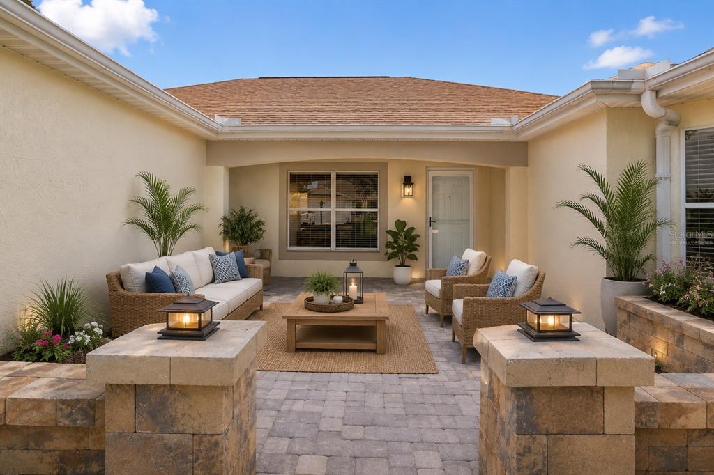 A furnished outdoor patio features a paver floor, stone walls, and a covered seating area — 1213 EL ESPARZA LANE, THE VILLAGES, FL