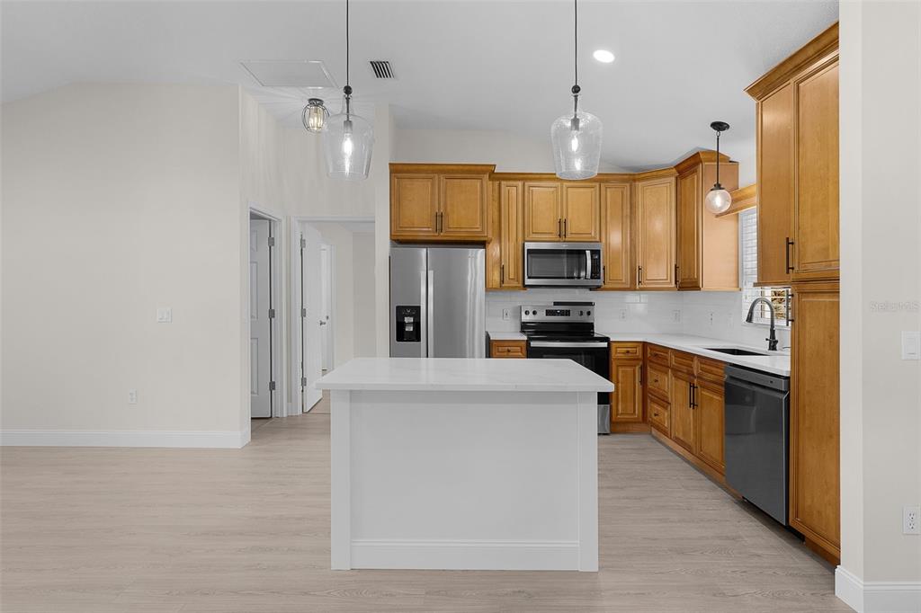 A kitchen features wood cabinets, a white island, stainless steel appliances, and light wood flooring — 1213 EL ESPARZA LANE, THE VILLAGES, FL