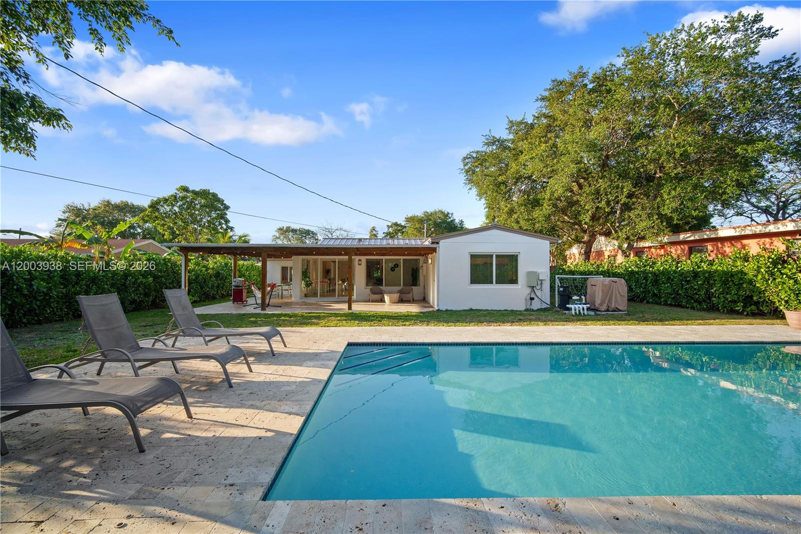 A backyard features a swimming pool, lounge chairs, and a covered patio attached to a house — 1360 NE 138th St, North Miami FL 33161, NORTH MIAMI, FL